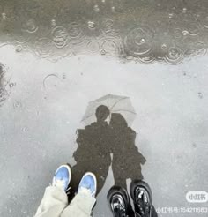 two people standing under an umbrella in the rain with their feet up on the ground