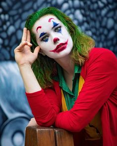 a woman with green hair and clown makeup is posing for a photo in front of a wall