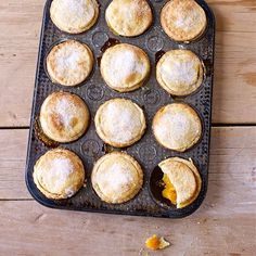 a muffin tin filled with mini pies on top of a wooden table next to an orange peel