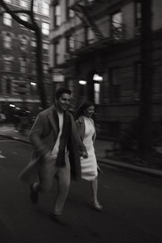 a man and woman are walking down the street at night, with buildings in the background