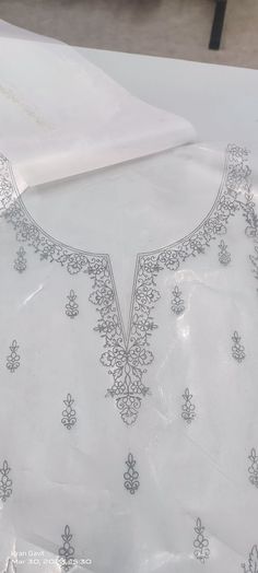 the back of a white dress with silver embroidery on it and a piece of paper next to it