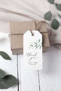 a tag that says thank you on it next to some green leaves and a brown box