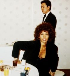 a woman sitting at a table with a man standing behind her in a suit and tie