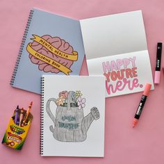 three notebooks and markers on a pink surface with some writing supplies next to them