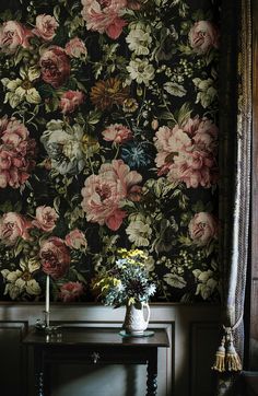 a vase with flowers on a table in front of a floral wallpapered wall