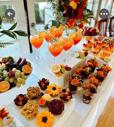 an assortment of snacks and drinks on a table with oranges, grapes, and flowers