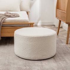 a living room with a bed and a white round footstool on the floor