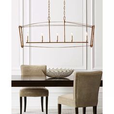 a chandelier hanging over a dining room table with chairs and a bowl on it