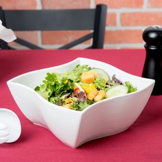 a white bowl filled with salad sitting on top of a red table cloth next to a black pepper shaker