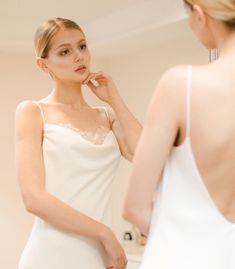 a woman in a white dress looking at herself in the mirror