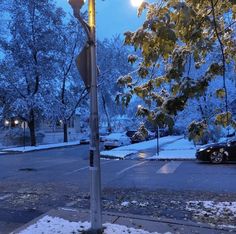 a street light with snow on the ground and cars parked in the lot behind it