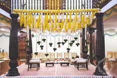 an indoor wedding setup with yellow flowers and greenery on the ceiling, hanging from black pillars