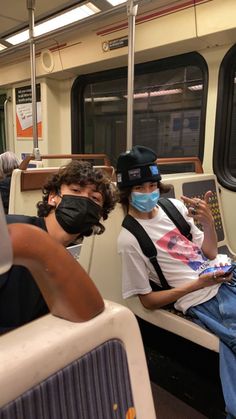 two people sitting on a train with masks on and one person wearing a face mask