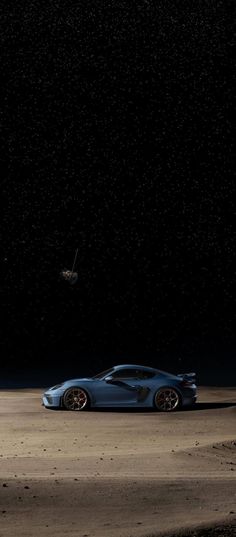 a blue sports car parked on top of a dirt field under a dark sky with stars