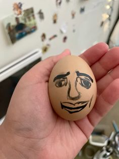 a hand holding an egg with a face drawn on it