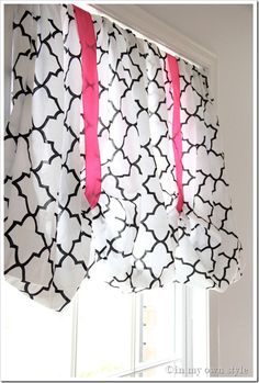 a window with pink ribbon hanging from it's valance and black and white curtains