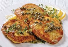 two pieces of fried fish on a plate with lemon wedges and garnishes