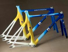 three blue and yellow bicycle frames sitting next to each other on a tile floor in front of a wall