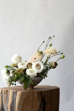 white flowers in a vase sitting on top of a wooden stump