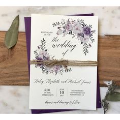 a purple and white wedding card with flowers tied to it on a piece of wood