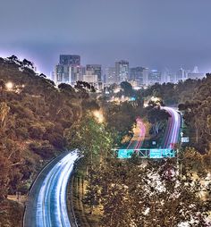 the city skyline is lit up at night as traffic passes by on an elevated highway