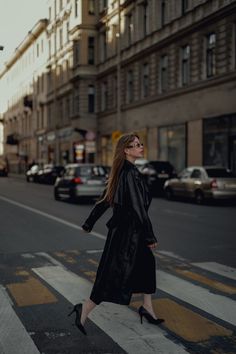 a woman walking across a cross walk in the middle of a city with tall buildings