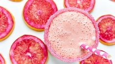 a pink drink in a glass surrounded by cut up grapefruits on a white surface