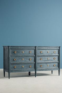 two blue dressers with gold knobs against a blue wall in an empty room