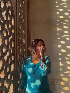 a woman standing in front of a wall with her hand on her face and looking at the camera