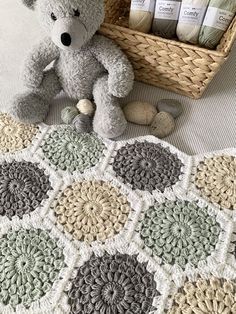 a teddy bear sitting on top of a bed next to a crocheted blanket