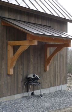 a grill sits under a wooden structure on the side of a building with a metal roof