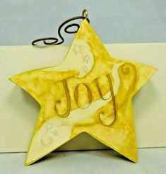 a yellow ceramic star ornament with the word joy written in cursive writing