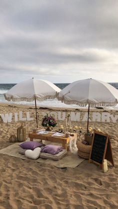 an umbrella is set up on the beach with pillows and blankets in front of it