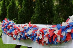 red, white and blue streamers on a table at an outdoor event with trees in the background