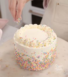 a person decorating a cake with sprinkles