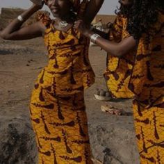 two women dressed in yellow and brown are standing on some rocks with their hands together