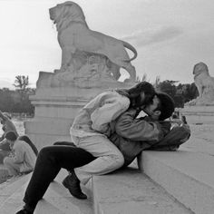 a man and woman sitting on the edge of a wall next to a lion statue