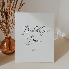 there is a sign that says bubbly bar next to a vase with dry grass