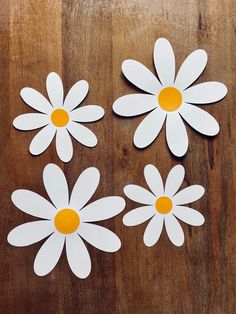 four white paper flowers with yellow centers on a wooden surface, cut out to look like daisies