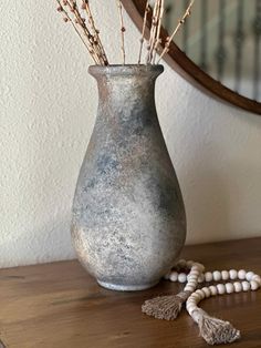 a vase sitting on top of a wooden table next to a beaded necklace and mirror