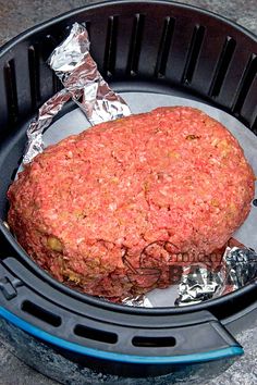 a large hamburger sitting inside of a black container on top of a counter next to aluminum foil