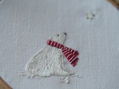 a white polar bear with a red scarf on it's head is embroidered onto a piece of fabric