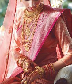 a woman in a red and gold bridal outfit with jewelry on her neck, sitting down