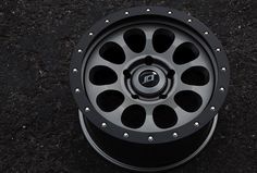 a black wheel on the ground with holes in it's center and spokes