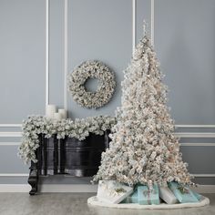 a white christmas tree sitting on top of a table next to a piano and wreath