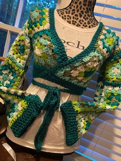 a crocheted top with green and white flowers on it, sitting on a mannequin