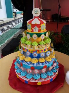 a large multi layer cake with cupcakes on the top and circus theme decorations