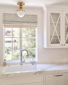 a kitchen with white cabinets and marble counter tops, gold faucet over the sink