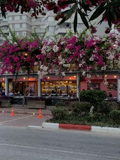 an empty parking lot with flowers growing on the building and people sitting at tables outside