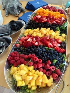 a platter filled with lots of fruit on top of a table next to plates and utensils